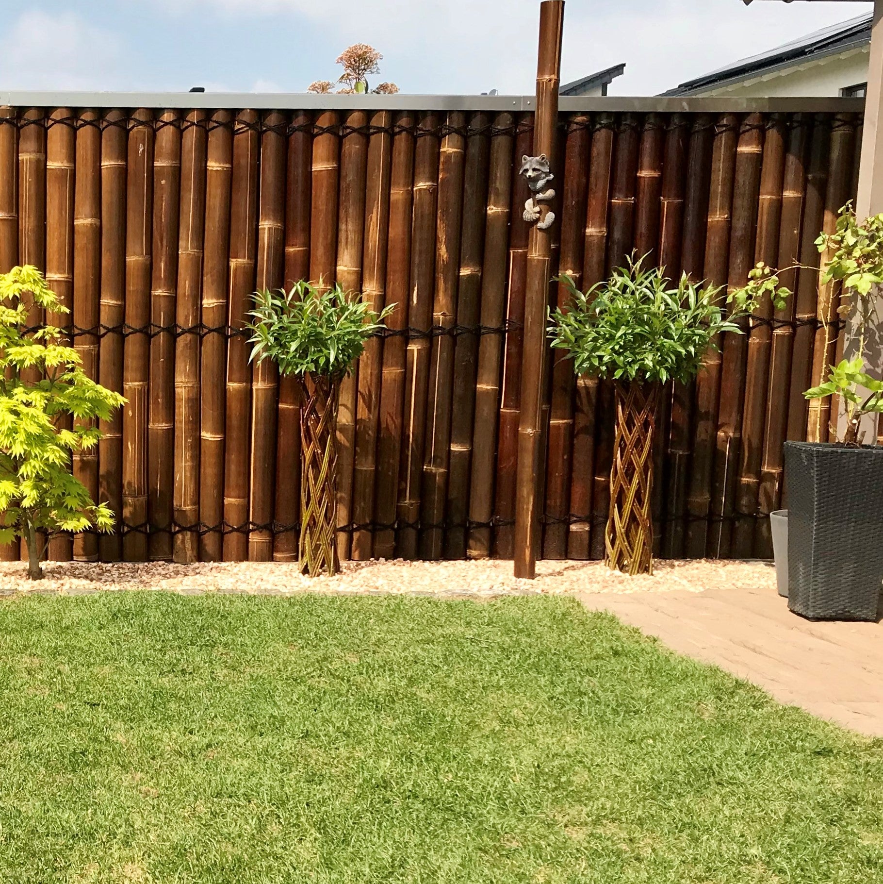 Garten mit dem Sichtschutz oder Wandverkleidung aus halben braunen Bambusrohren mit Kokosschnürung als Dekoration