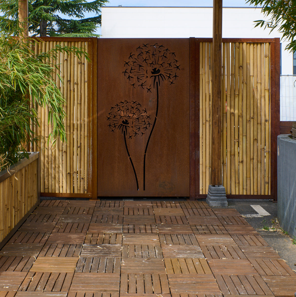 Bambuszaun mit integrierter Motivwand aus Cortenstahl mit Pusteblumenmotiv als dekorativer Sichtschutz im Garten.