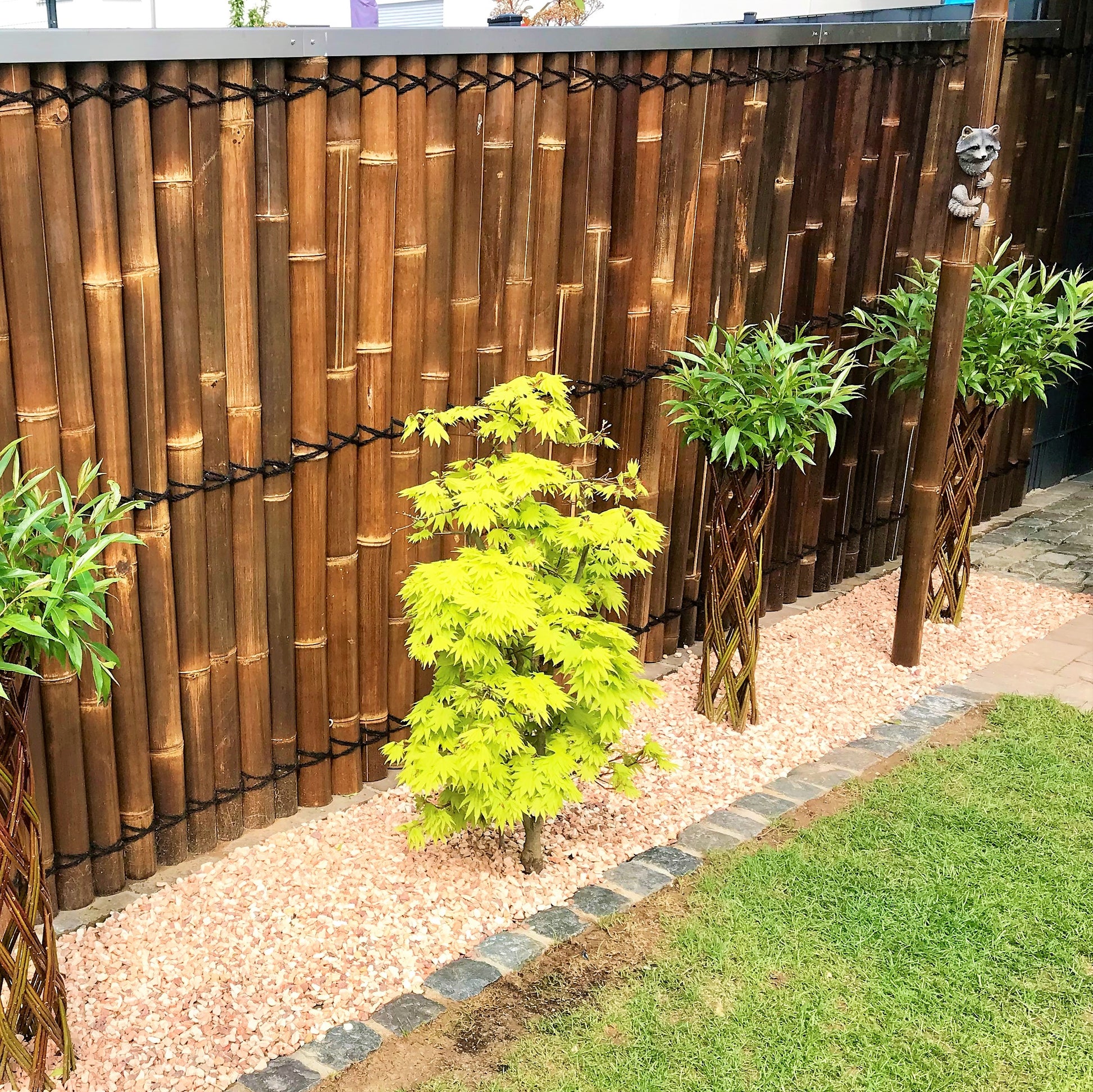 Garten mit dem Sichtschutz oder Wandverkleidung aus halben braunen Bambusrohren mit Kokosschnürung als Dekoration